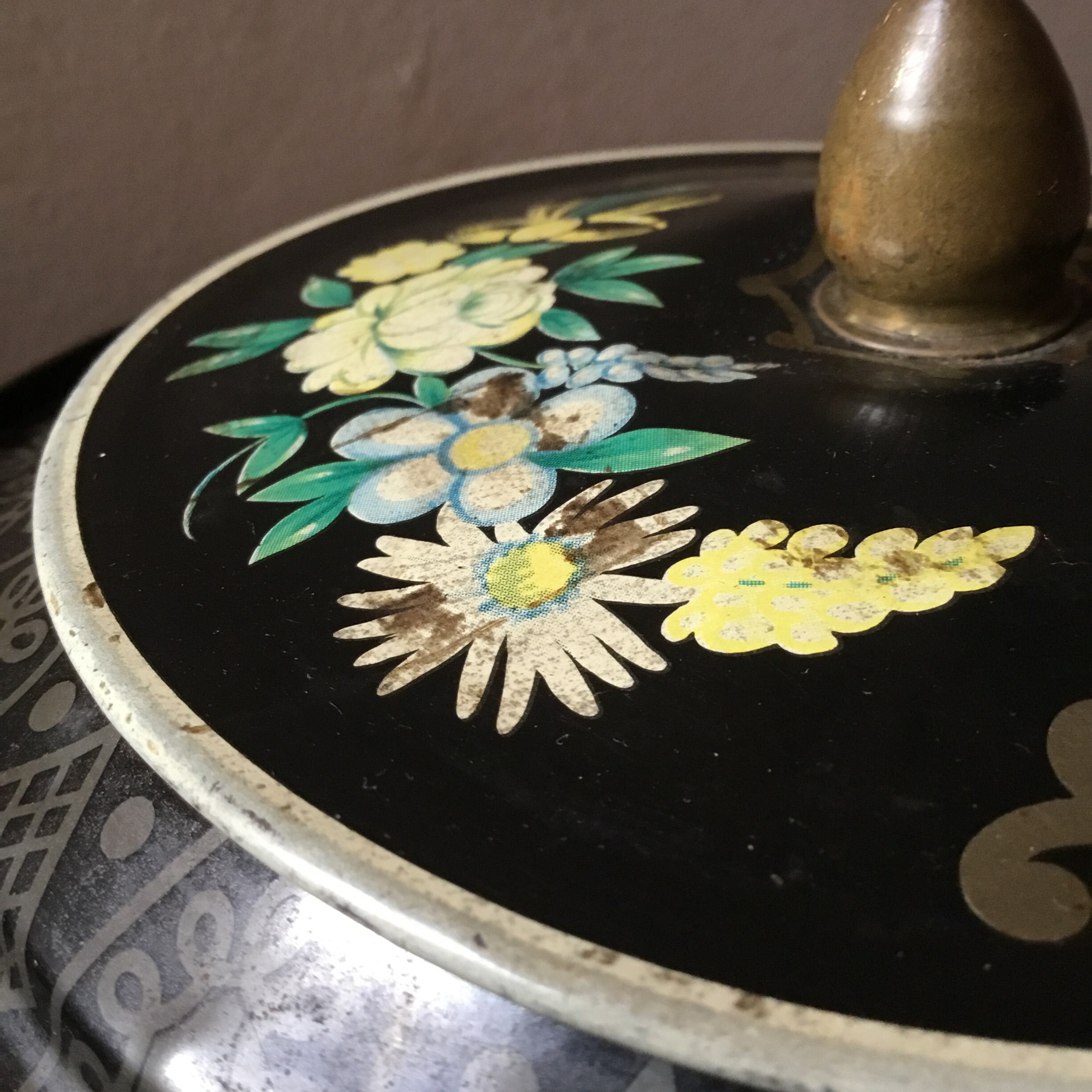 ヴィンテージアンティークの丸型花柄ブリキ缶。黒地に花柄が描かれてい