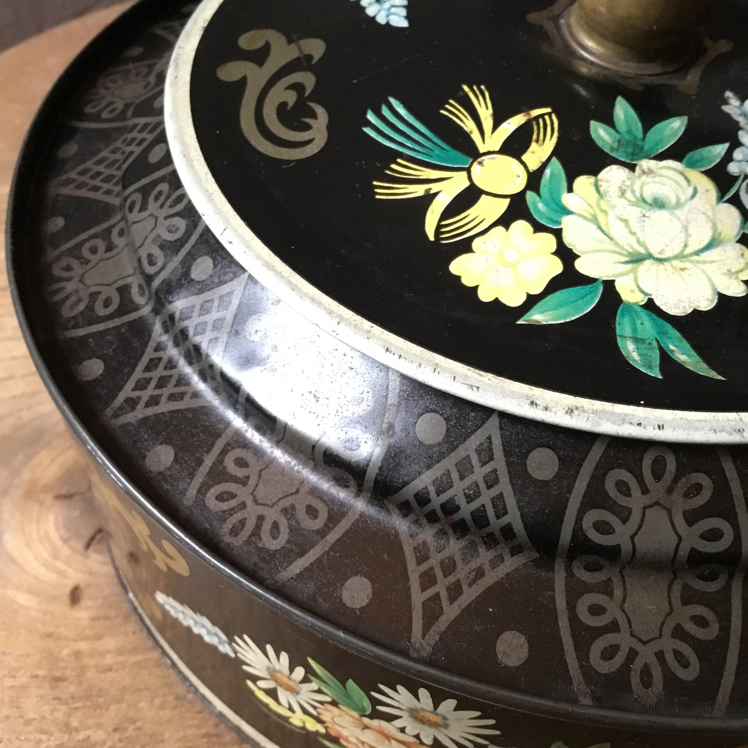 ヴィンテージアンティークの丸型花柄ブリキ缶。黒地に花柄が描かれてい