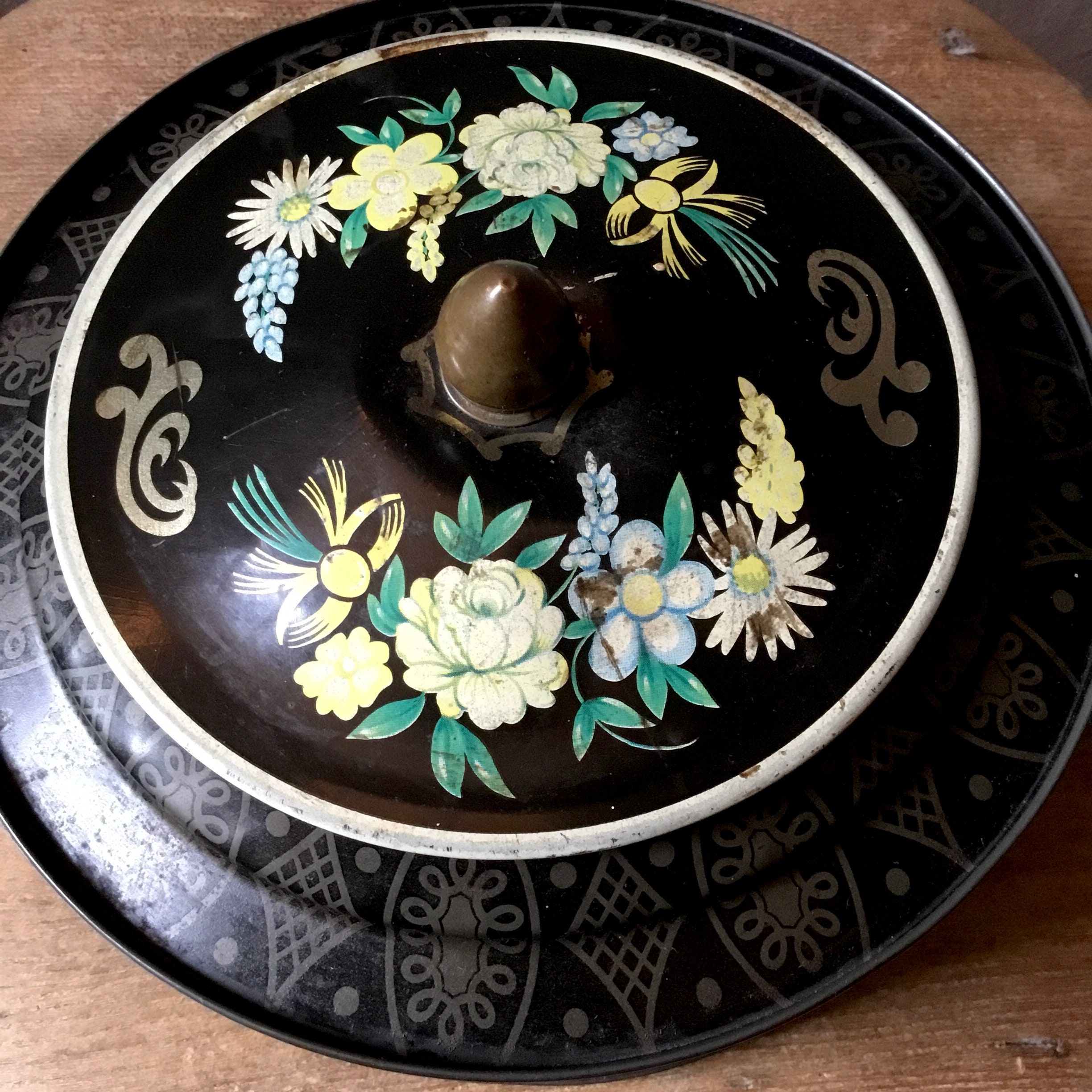 ヴィンテージアンティークの丸型花柄ブリキ缶。黒地に花柄が描かれてい