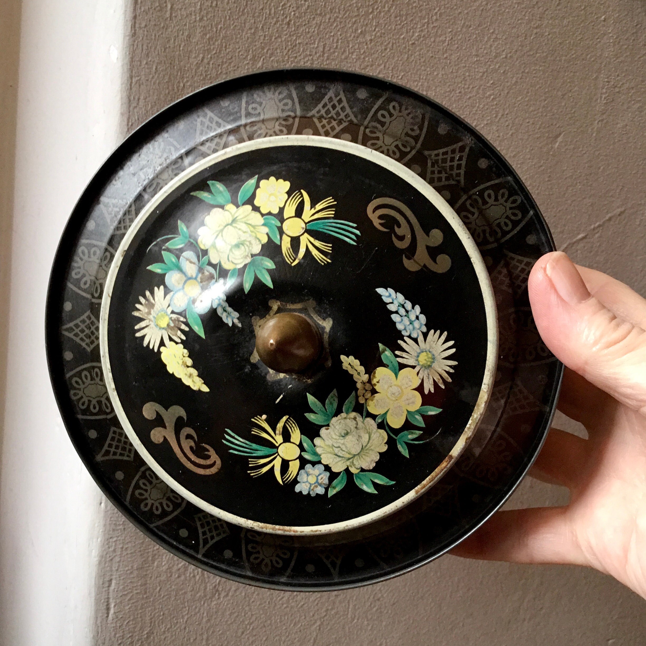 ヴィンテージアンティークの丸型花柄ブリキ缶。黒地に花柄が描かれてい