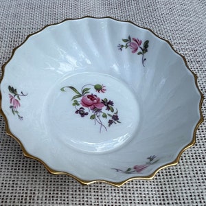 May include: A white porcelain bowl with a gold rim and floral designs. The bowl has a scalloped edge and features pink and purple flowers.