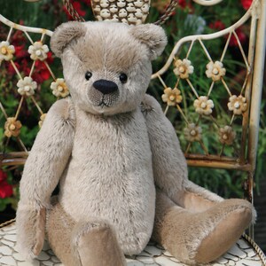May include: A beige teddy bear with black eyes and a black nose sits on a white chair with a metal frame. The chair is decorated with white flowers.