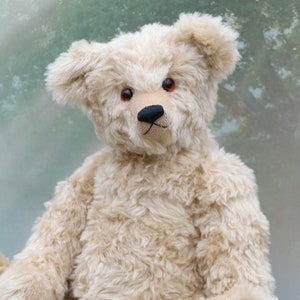 May include: A cream-colored teddy bear with red button eyes and a black nose sits on a wooden surface. The bear has a fluffy, soft texture.