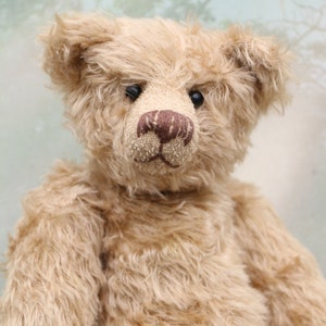 May include: A vintage teddy bear with a light brown fur coat. The bear has black eyes, a brown nose, and a stitched mouth.