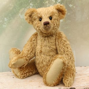 May include: A light brown teddy bear with a fluffy coat, sitting with its legs crossed. The bear has black eyes, a brown nose, and a stitched smile.