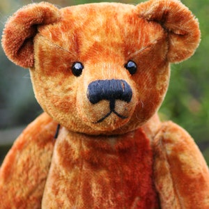 May include: A close-up of a brown teddy bear with a black nose and button eyes. The bear has a worn, vintage look and is made of soft, plush fabric.