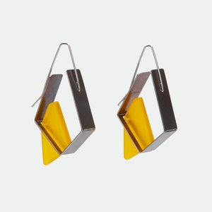 May include: A pair of modern earrings featuring a geometric design. Each earring has a silver-tone metal frame in a square shape, with a bright yellow, triangular insert. The earrings hang from a simple silver-tone wire.