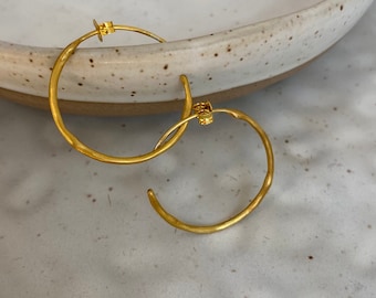 May include: A pair of gold hoop earrings with a hammered texture.