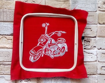 May include: White embroidered motorcycle design on a red fabric background. The motorcycle is in a white embroidery hoop.