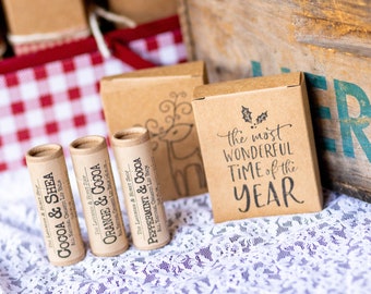 May include: Three cardboard tubes of lip balm with the labels "Cocoa & Shea", "Orange & Cocoa", and "Peppermint & Cocoa". The tubes are sitting on a white lace tablecloth next to a small cardboard box with the text "the most wonderful time of the year".