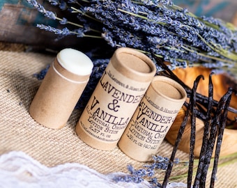 May include: Two brown cardboard tubes with white lids containing lavender and vanilla scented lotion sticks. The tubes are labeled "Lavender & Vanilla Natural Organic Lotion Stick". The image also shows dried lavender flowers and vanilla beans.