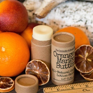 May include: A brown cardboard tube with a white label that reads "The Lavender & Honey Shop Orange Mango Butter All-Natural Organic Lotion Stick 2.37 fl oz www.thelavenderandhoneyshop.com". The tube is sitting on a wooden surface with oranges, dried orange slices, and a wooden ruler.