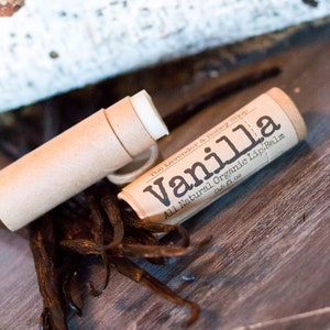 May include: A brown cardboard tube with a white lip balm inside. The tube is labeled "Vanilla All Natural Organic Lip Balm 0.15 fl oz The Lavender & Honey Shop".