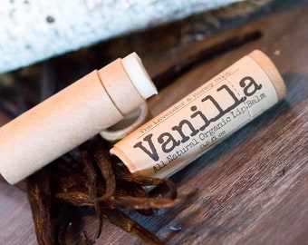 May include: A brown cardboard tube with a white lip balm inside. The tube is labeled "Vanilla All Natural Organic Lip Balm 0.15 fl oz The Lavender & Honey Shop".