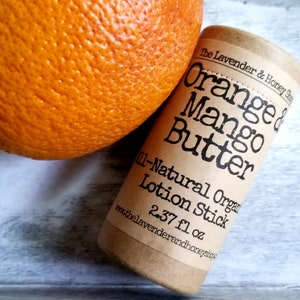 May include: A brown cardboard tube with a white label that reads "The Lavender & Honey Shop" and "Orange & Mango Butter 11-Natural Organic Lotion Stick 2.37 fl oz"  The tube is next to a bright orange, textured orange.