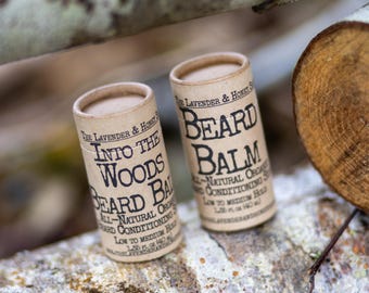 May include: Two cylindrical cardboard tubes of beard balm with tan labels and black text. The labels read The Lavender & Honey Shop, Into The Woods Beard Balm, All-Natural Organic Beard Conditioning Salve, Low to Medium Hold, 1.55 oz (40 g).