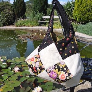 May include: A patchwork tote bag with a black, white, and gold floral design. The bag has a large, open top and two long straps.