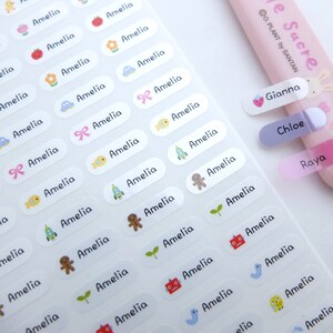 May include: A sheet of white oval-shaped stickers with the name Amelia printed on each sticker. Each sticker has a different cartoon image, including a chick, a flower, a car, a bow, a fish, a rocket, a gingerbread man, a sprout, a robot, a bird, and a chick. There are also three rectangular stickers with the names Gianna, Chloe, and Raya printed on them.