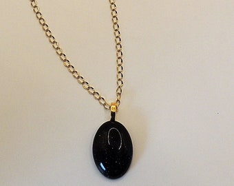 May include: A gold chain necklace with a black oval pendant. The pendant has a sparkly, glittery texture.