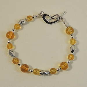 May include: A silver and amber beaded bracelet with a heart-shaped clasp. The bracelet features alternating round amber beads and silver beads with a textured design.