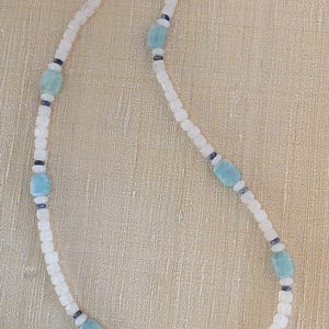 Könnte beinhalten: Eine weiße und blaue Perlenkette mit einem silbernen Verschluss. Die Kette hat hellblaue quadratische Perlen und dunkelblaue runde Perlen.