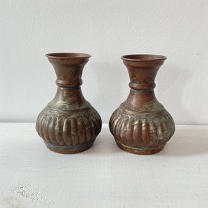 May include: A pair of small, copper vases with a textured, ribbed design. The vases have a slightly aged, greenish patina.