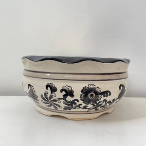 May include: A white ceramic planter with a black floral design. The planter has a scalloped rim and a wide, round base.
