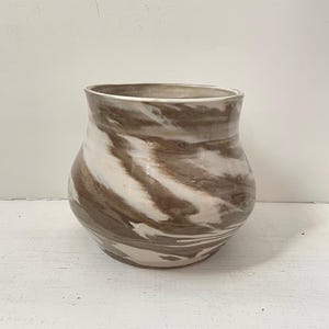 May include: A handcrafted ceramic vase with a wide, rounded body and a slightly flared rim. The vase features a marbled design of brown and white swirls, creating a unique and organic aesthetic. The vase is suitable for displaying flowers or as a decorative accent.