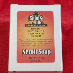 May include: A white rectangular box of Neroli Soap with an orange and yellow gradient label. The label features the Sands Inc. logo, address in Arkansas City, KS, ingredient list, and the text Net.Wt. 5 oz. and 147.8 ml. printed on the front.