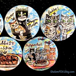 May include: A set of six colorful round buttons with images of cats and a loaf of bread. The buttons feature the text "Mame", "Bubbe 1", "Bubbe 2", "Mishpocheh", "Bubbe's Babka", and "Shayna Punim".