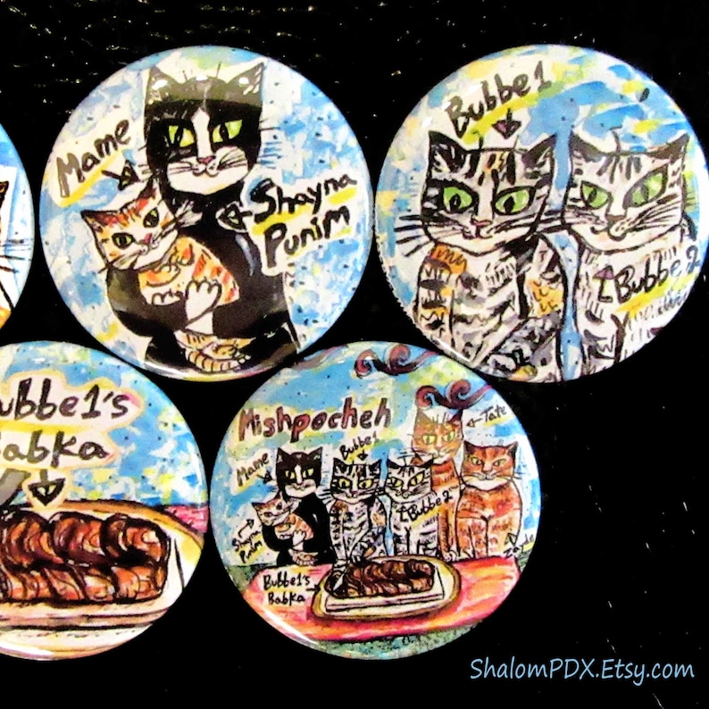 May include: A set of six colorful round buttons with images of cats and a loaf of bread. The buttons feature the text "Mame", "Bubbe 1", "Bubbe 2", "Mishpocheh", "Bubbe's Babka", and "Shayna Punim".