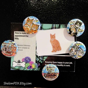 May include: Five colorful round magnets with painted images of cats. The magnets feature different cat breeds and names, including Zayde, Tate, Mame, Shayna, Punim, and Bubbe. The magnets are on a black background with a white card that says "Time to make an appointment for Kitty." and "Keeping them happy is your job. Keeping them healthy is ours."
