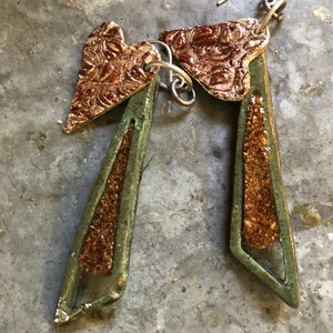 Puede incluir: Un par de pendientes hechos a mano con un dije en forma de corazón y un diseño geométrico. Los pendientes están hechos de arcilla verde y marrón con un acabado texturizado.