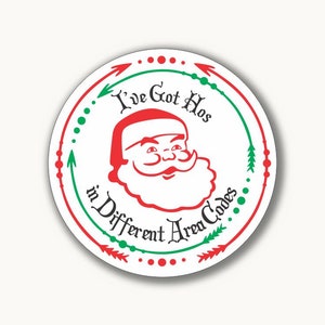 Könnte beinhalten: Ein weißer Kreis mit grünem und rotem Rand. Der Kreis enthält ein Cartoon-Bild vom Weihnachtsmann mit dem Text "I've Got Hos in Different Area Codes".