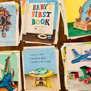 May include: A collection of vintage children's book pages. The pages feature colorful illustrations of a cuckoo clock, a mirror, a plane, a train, and other objects. One page is titled "Baby's First Book."