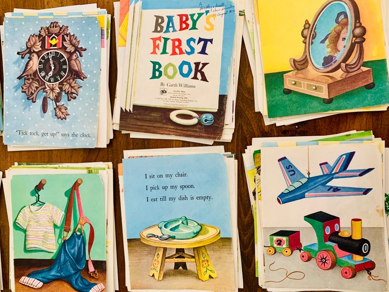 May include: A collection of vintage children's book pages. The pages feature colorful illustrations of a cuckoo clock, a mirror, a plane, a train, and other objects. One page is titled "Baby's First Book."