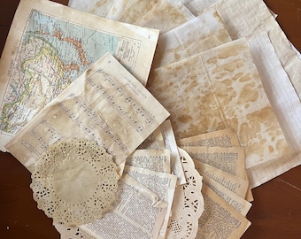 May include: A collection of vintage ephemera, including aged paper, maps, sheet music, and doilies. The papers have a warm, aged appearance with brown stains. The items are arranged on a dark wooden surface, creating a nostalgic aesthetic.