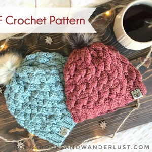 May include: Two crocheted hats with faux fur pom poms. One hat is blue and the other is red. The hats are on a wooden surface with string lights and snowflakes.