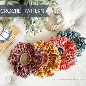 May include: Four crocheted hair scrunchies in different colors: burgundy, mustard yellow, coral pink, and teal blue. The scrunchies are arranged in a circle on a white surface. The text "@HOOKSBOOKSWANDERLUST" is visible in the bottom right corner of the image.