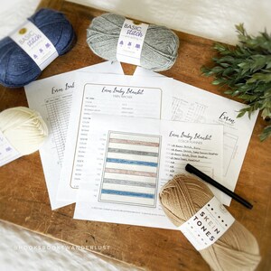 May include: A close-up of a yarn colour planner for a crochet baby blanket project. The planner includes a yarn tracker and colour chart with different shades of blue, grey, and pink yarn. The image also shows several skeins of yarn in various colours, including beige, blue, and grey.
