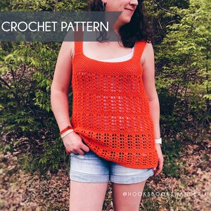 May include: A crochet tank top in a bright orange color with a lacy pattern. The top is sleeveless and has a square neckline. The model is wearing the top with denim shorts and is standing in a wooded area.