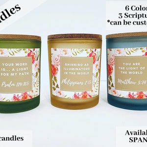 Puede incluir: Tres velas de 85g en verde, dorado y azul, cada una con una etiqueta floral y un versículo bíblico. Las velas tienen tapas de corcho y están etiquetadas con el texto "Candles". El texto "6 colores 3 escrituras" también es visible.
