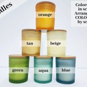May include: Six candles in frosted glass jars with wooden lids. The candles are arranged in a pyramid shape, with the top candle being orange, the next row being tan and beige, and the bottom row being green, aqua, and blue. The text "Colors vary in scents Arranged by COLOR, not by scent" is written in black text on a white background.