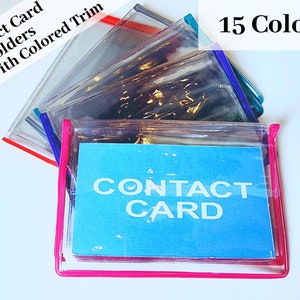 May include: A stack of clear plastic contact card holders with colored trim. The top holder has a pink trim and a blue card inside that says "CONTACT CARD". The text "15 Colors" is visible in the top right corner of the image.