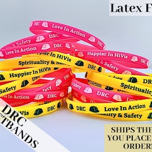 May include: A stack of colorful silicone wristbands with different messages, including "Love In Action", "Happier In HiVis", and "Spirituality & Safety". The wristbands are yellow, pink, and red with black lettering. The text "DRC Wristbands" is visible in the lower left corner of the image.