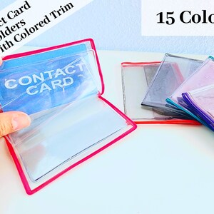 May include: Clear plastic contact card holders with colored trim. The holders are open and show the words "Contact Card" printed on the inside. There are 15 different colors available.