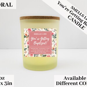 May include: A 3 ounce candle with a floral design and the text "Smells Like You're Getting Baptized!"  The candle is in a clear glass jar with a cork lid. The candle is available in different colors.