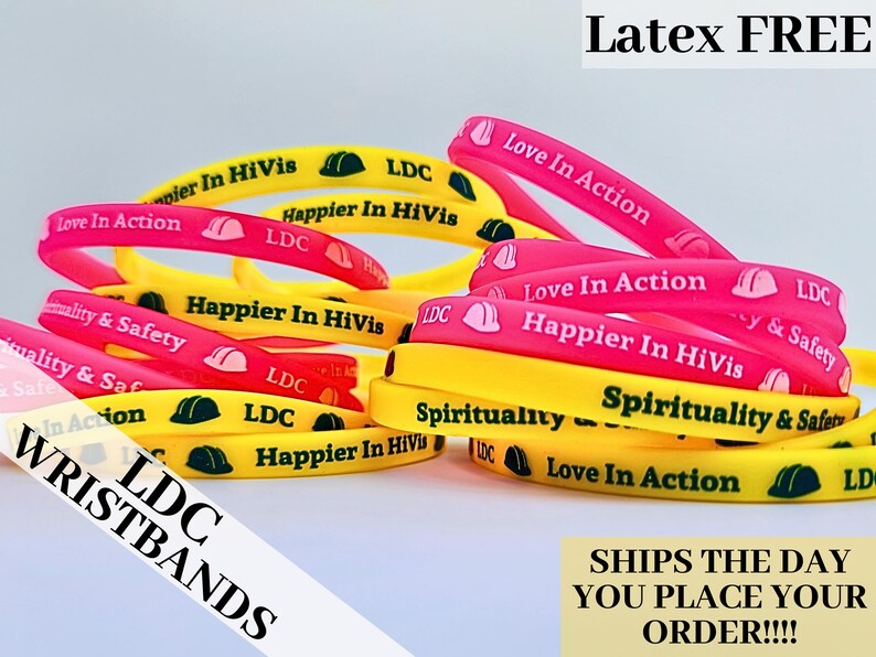 May include: A close-up of a pile of colorful silicone wristbands with various messages, including "Love In Action", "Happier In HiVis", "Spirituality & Safety", and "LDC".