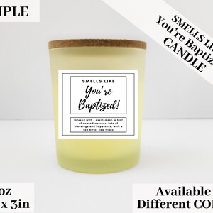 May include: A 3 ounce candle with a yellow glass jar and a cork lid. The label reads "Smells Like You're Baptized!" and is decorated with a black and white design. The candle is available in different colors.