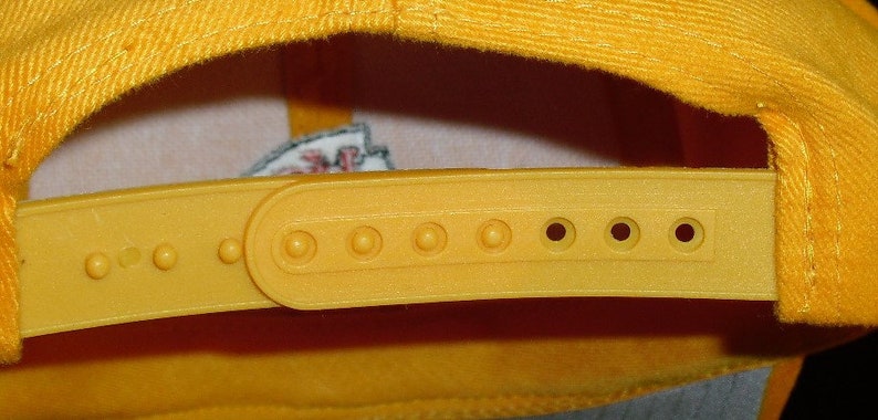 May include: A yellow baseball cap with a yellow adjustable strap and a row of holes for adjusting the size. The strap is made of a smooth, plastic-like material.
